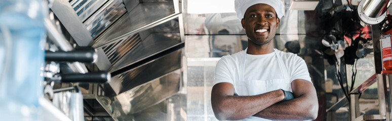 panoramic shot of positive african american chef standing with crossed arms in food truck - Powered by Adobe