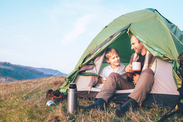 Father and son sit in camp tent drink hot tea and have conversation. Leisure time with father,...