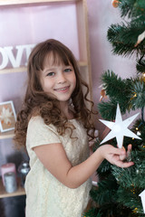 Merry Christmas, happy holidays! Family holiday. Happy New Year 2020. Girl enjoys the holiday and decorates the Christmas tree. Cute little girl hangs a Christmas star on a Christmas tree. Winter.