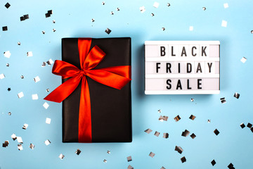Lightboard with letters and black gift box with red ribbon. Black friday sale concept.