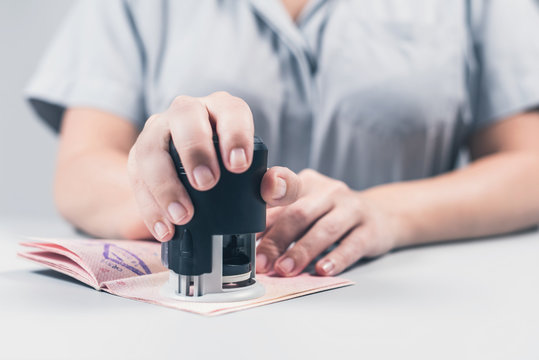 Immigration And Passport Control At The Airport. Woman Border Control Officer Puts A Stamp In The Passport. Concept