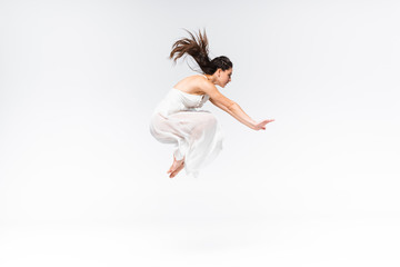 side view of young beautiful ballerina jumping while dancing on grey background