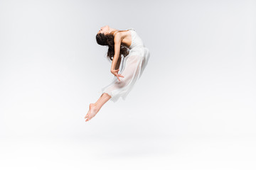 Side view of graceful young ballerina jumping in dance on grey background