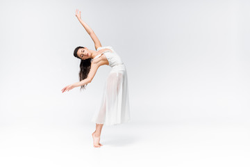 Fototapeta na wymiar beautiful ballerina in white dress dancing with closed eyes on grey background