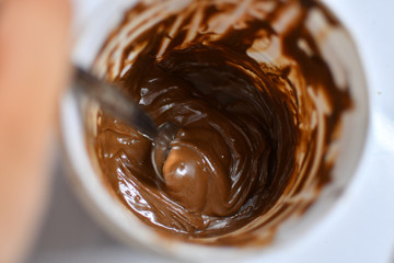 Spoon taking chocolate cream out of the white plastic jar