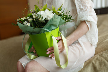 bride holds aflowers in bright packaging indoor. young girl in white dress with a delicate festive  bouquet .holiday flower arrangement.beautifully packaged flowers as a gift in women's hands indoor