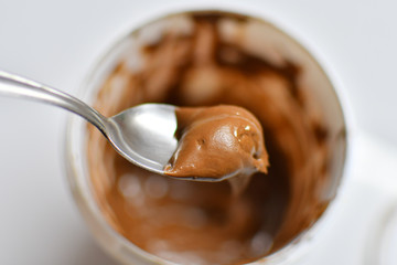 Spoon taking chocolate cream out of the white plastic jar