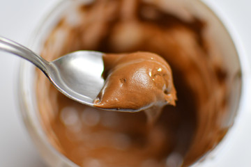 Spoon taking chocolate cream out of the white plastic jar