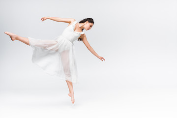 Obraz premium attractive young ballerina dancing in white dress on grey background