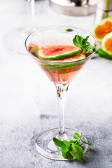 Pink fig martini cocktail in shot glass on gray table with bar tools, selective focus