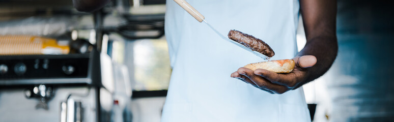 panoramic shot of afrian american man holding spatula while preparing burger