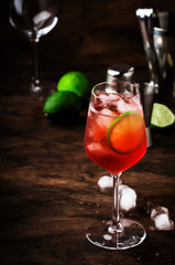 Campari tonic alcoholic cocktail with red bitter, tonic, lime and ice. Old wooden table background, bar tools, selective focus. All names refer to cocktails, not trademarks