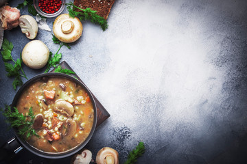 Autumn or winter meat vegetable mushroom hot soup with beef and wholegrain barley. With black breaв and parsley, top view, gray kitchen table, copy space