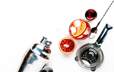 Negroni alcoholic cocktail with dry gin, red vermouth and red bitter, bloody orange slice and ice cubes. White background, steel bar tools, top view, copy space