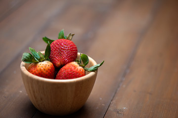Fresh strawberries in a bowl on wooden background