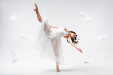 beautiful ballerina dancing surrounded with papers flying around on grey background