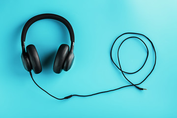 Black headphones with a wire on a blue background. View from above. In-ear headphones for playing games and listening to music tracks