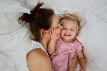 Fototapeta na wymiar Mother and her infant baby cuddling in the bed, adorable blonde baby and her mum having fun, happy family life concept