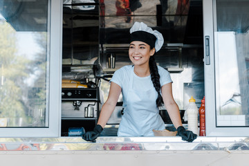 Happy Asian woman in hat and chef uniform smiling in food truck