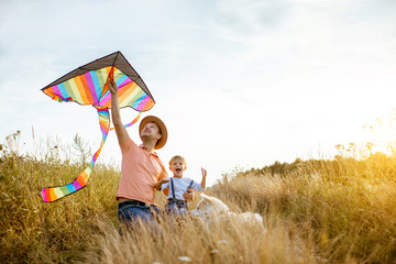 Portrait of a happy father and son holding colorful air kite while sitting together on the field during the sunset