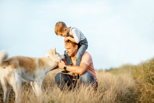 Portrait of a happy father with young son riding on the shoulders and their dog having fun on the field. Concept of a happy family on a summer activity