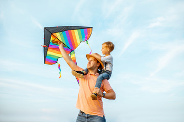 Portrait of a happy father and young son on the shoulders with colorful air kite on the blue sky...