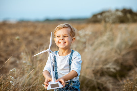 Curious young boy playing with toy wind turbine in the field, studying how green energy works from a young age