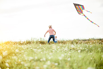 Father with son launching colorful air kite on the field during the sunset. Concept of a happy family having fun during the summer activity