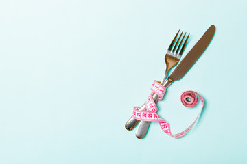 Crossed fork and knife are wrapped in measuring tape on blue background. Concept of diet for weight...