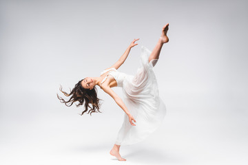young beautiful ballerina in white dress dancing on grey background