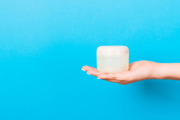 Female hand holding cream bottle of lotion isolated. Girl give jar cosmetic products on blue background