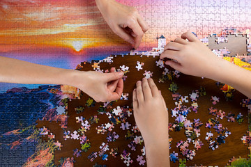 children and adult hands stack color puzzle on wooden table - obrazy, fototapety, plakaty