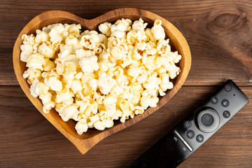 Heart shaped popcorn in a wooden bowl and a television remote control on a wooden table