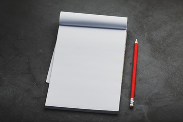 Notebook with a red pencil on a dark background for writing. Free empty space for writing on a blank sheet of a notebook,