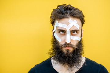 Close-up portrait of an injured man with medical patches on his face on the yellow baackground