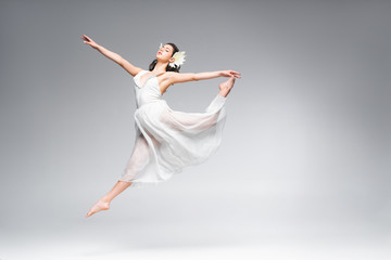 beautiful young ballerina in white dress dancing on grey background