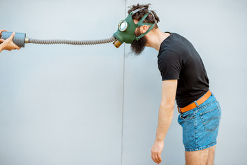 Portrait of a man with gas mask, pulling the pipe on the grey background. Concept of poor ecology,...