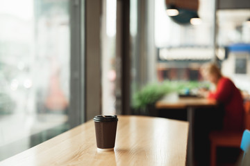 picture of brown paper cup with hot coffee drink standing on the wooden table in the cafe