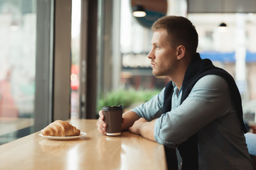 young handsome man having his croissant and drinking hot coffee for lunch in the cafe