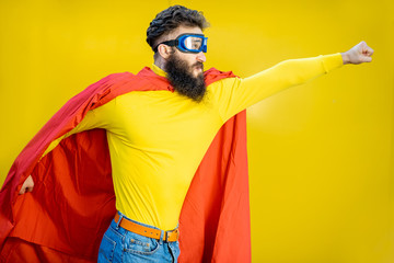 Portrait of a man like a superhero in colorful clothes and pilot's glasses on the yellow background