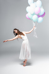 young attractive ballerina in white dress dancing with festive balloons on grey background