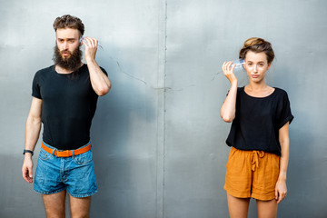 Man and woman talking with string phone made of cups on the gray background. Concept of...