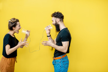 Man and woman talking with string phone, shouting on each other on the yellow background. Concept...