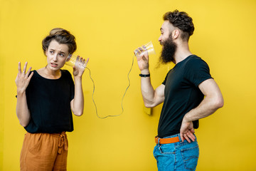 Man and woman talking with string phone made of cups on the yellow background. Concept of...
