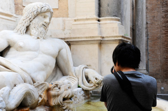 Marphurius or Marforio talking statues of Rome with an asian visitor taking a photo. Rome, Italy