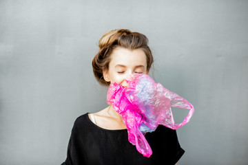 Portrait of a young woman suffocated of plastic bags on the grey background. Concept of non-recyclable plastic pollution