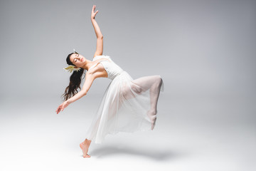 Naklejka premium beautiful young ballerina in white dress dancing on grey background