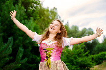  young woman in dirndl standing outdoors and spreading her arms