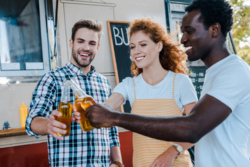 selective focus of happy multicultural men clinking with redhead woman near food truck