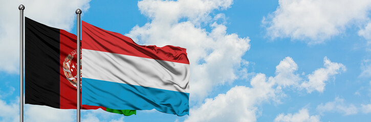 Afghanistan and Luxembourg flag waving in the wind against white cloudy blue sky together....